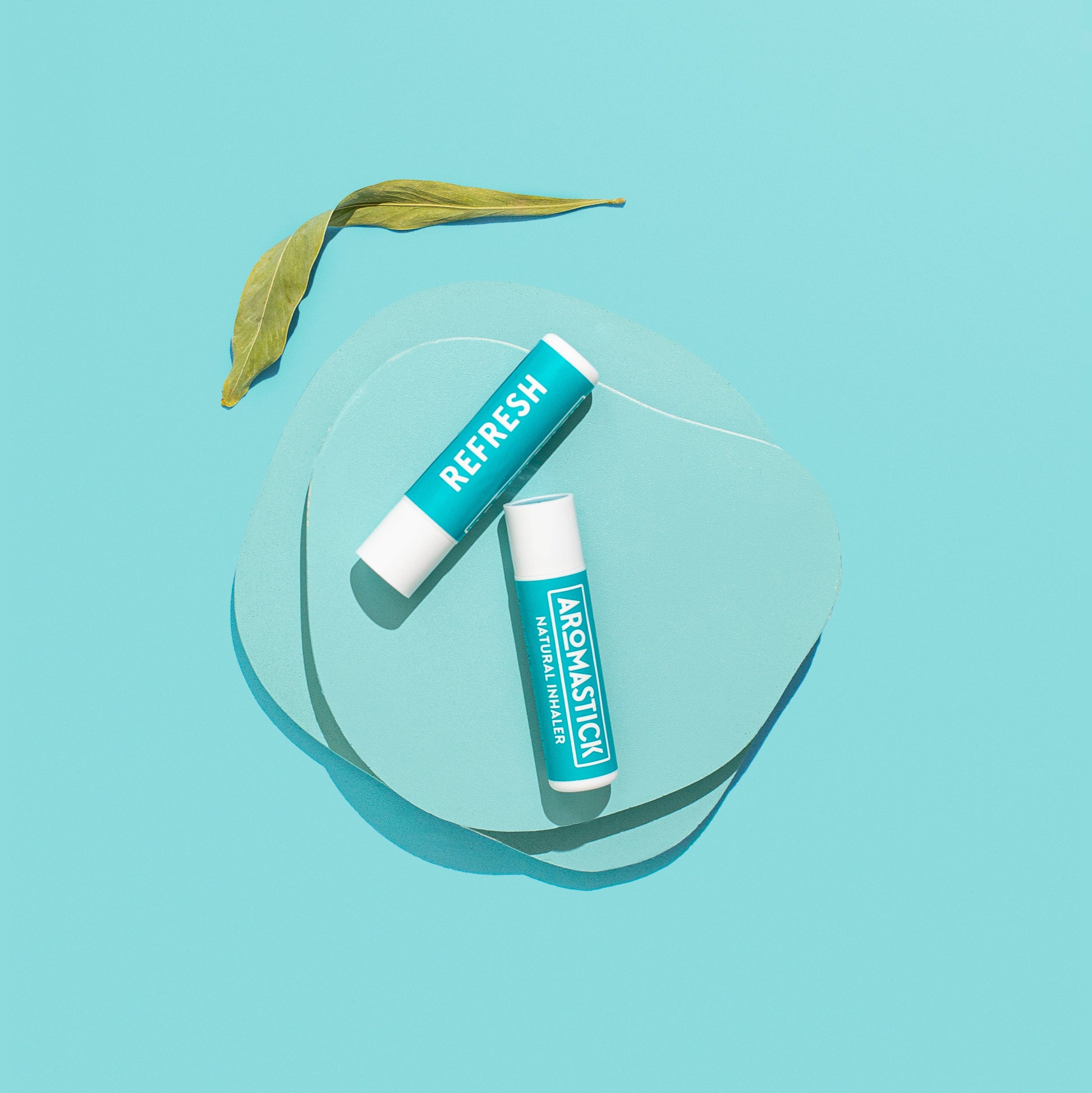 Two natural inhaler tubes labeled 'Refresh' on a clear glass surface with a light blue background.